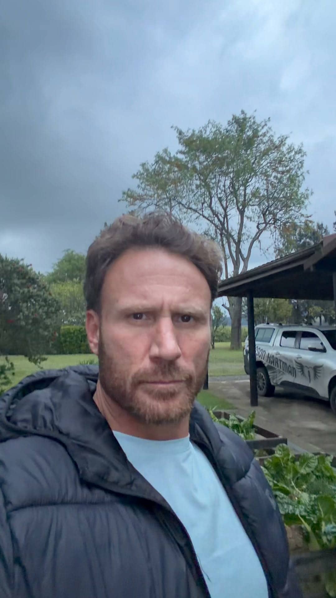 Jason Hartman beside raised vegetable beds under a grey sky, his branded bakkie parked behind him